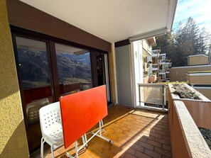 A balcony with a white chair, a red table, and a view of a mountain. - Lärchenwald 1808 # 4-bed apartment, Bad, WC 4-Bettwohnung, Bad, WC by Interhome (Leukerbad)