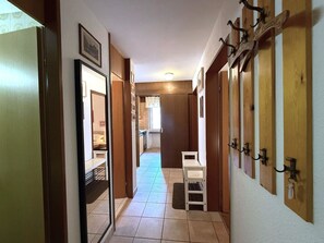 Un couloir avec un banc blanc, des portes en bois dotées de crochets en métal et un sol carrelé.