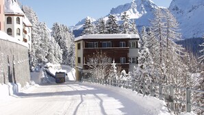 Una strada innevata con un edificio che presenta un balcone e una montagna sullo sfondo.