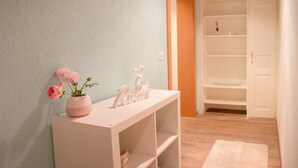 Una stanza con un tavolino da toilette bianco, un vaso rosa con fiori e una porta bianca che conduce a un armadio con scaffali.