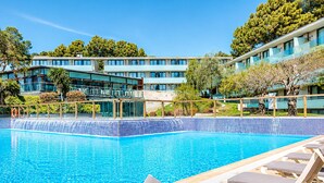 A swimming pool with lounge chairs, a building with multiple floors, and trees in the background. - Family Apartment by the Balearic Sea (Castell-Platja d'Aro)