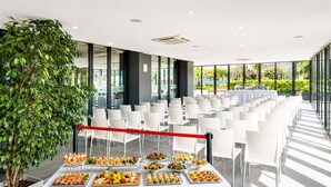 A conference room with a white table set with various food items, surrounded by white chairs, and a large potted plant. - Family Apartment by the Balearic Sea (Castell-Platja d'Aro)