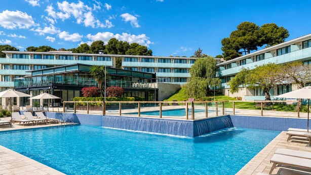 A swimming pool with lounge chairs and a modern building in the background. - Family Apartment by the Balearic Sea (Castell-Platja d'Aro)
