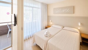 A hotel room with two beds, a balcony with a chair, a 'Welcome' sign, and a view of the outside. - Family Apartment by the Balearic Sea (Castell-Platja d'Aro)