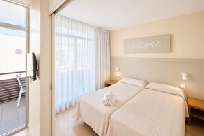 Ett hotellrum med två sängar, en balkong med en stol, en välkomstskylt och utsikt över omgivningarna.