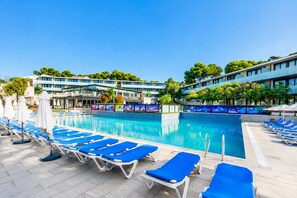 En swimmingpool med blå solstolar och parasoller, omgiven av en hotellbyggnad med modern design.