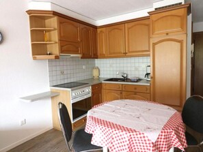 Eine kleine Küche mit Holdekor-Schränken, einem Herd, einer Spüle und einem Essbereich mit Tisch, der mit einer karierten Tischdecke bedeckt ist.