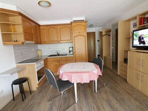 Eine kompakte Küche mit Holzausbau, einer gefliesten Spritzschutzwand, einem Esstisch mit Stühlen und einem Fernseher.