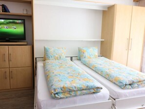 Ein Schlafzimmer mit zwei Einzelbetten, einem Fernseher auf einem Schrank und Holzschränken.