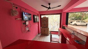 A room with pink walls, a ceiling fan, a television, a cabinet, and a window with a view of a car outside. - Hotel O Adamas University Barasat (Barasat)