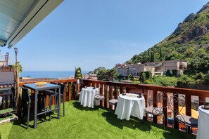 A terrace with tables and chairs, overlooking a coastal town and hills. - Apartment 'Le Grand Soleil - Albatros' with Sea View, Wi-Fi and Air Conditioning (Taormina)