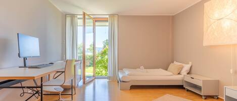 Une chambre d’hôtel moderne équipée d’un bureau, d’un ordinateur, d’une chaise, d’un lit, d’une table de chevet et offrant une vue sur la verdure.