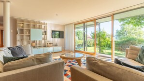 Un salon moderne avec un canapé, une table basse et un téléviseur. Une grande fenêtre offre une vue sur l’extérieur.