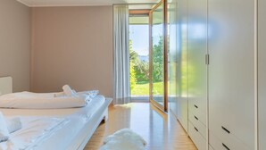 Une chambre à coucher avec un lit, une armoire blanche et une vue sur un jardin, visible à travers une porte vitrée.