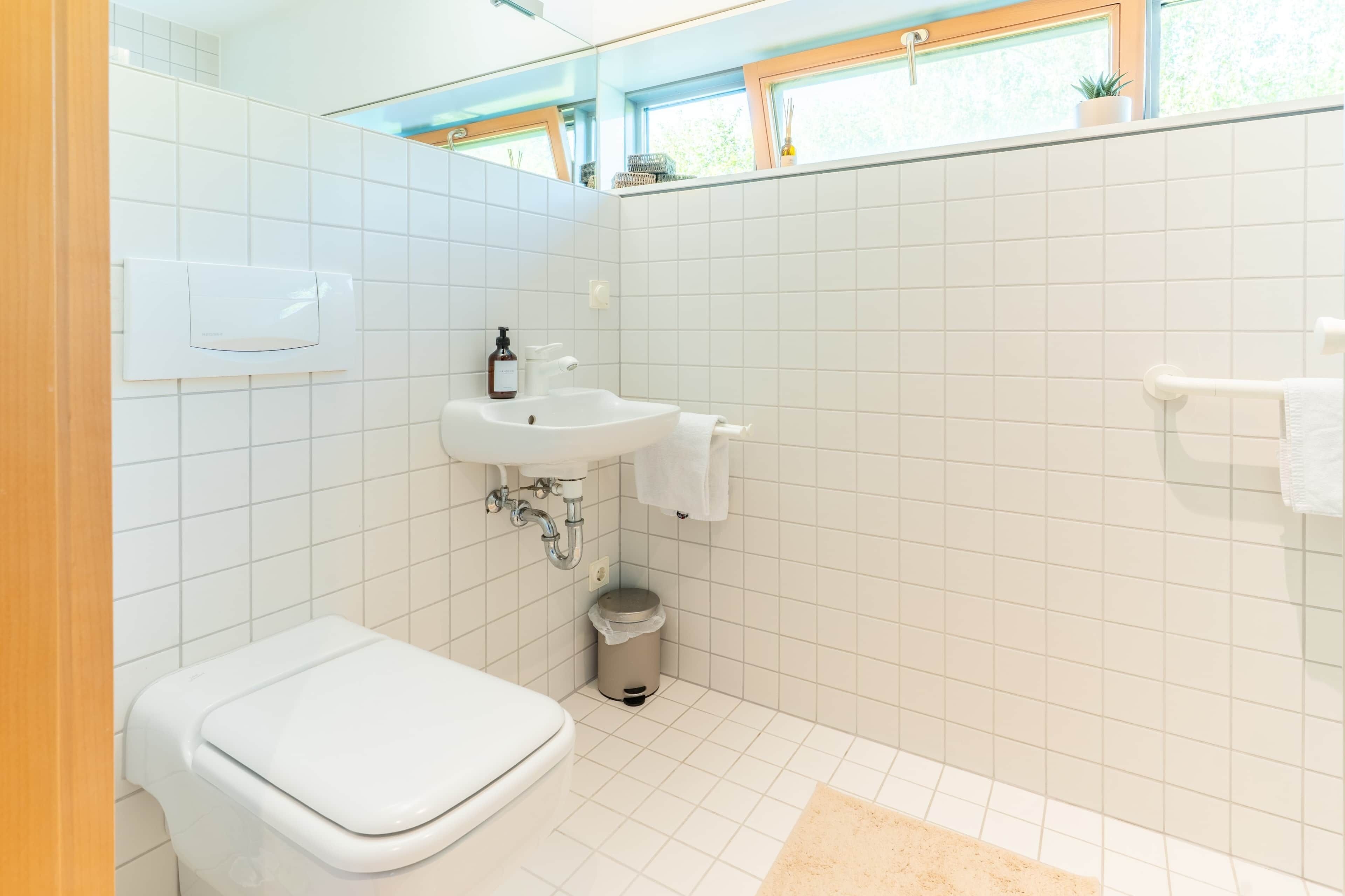 Une salle de bain avec des toilettes blanches, un lavabo et une petite poubelle.