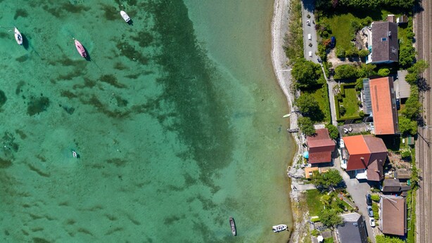 Vue aérienne d’une zone côtière avec des eaux cristallines, des bateaux et des immeubles résidentiels aux toits rouges.