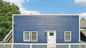 A two-story building with a blue exterior, white trim, and a balcony with white railings. - Loft Haven Rooftop Terrace (Charlotte)