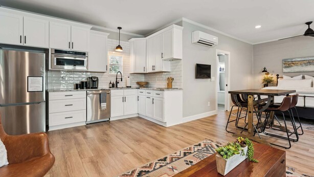 A modern kitchen with white cabinets, stainless steel appliances, and a dining area with a wooden table and chairs. - Loft Haven Rooftop Terrace (Charlotte)