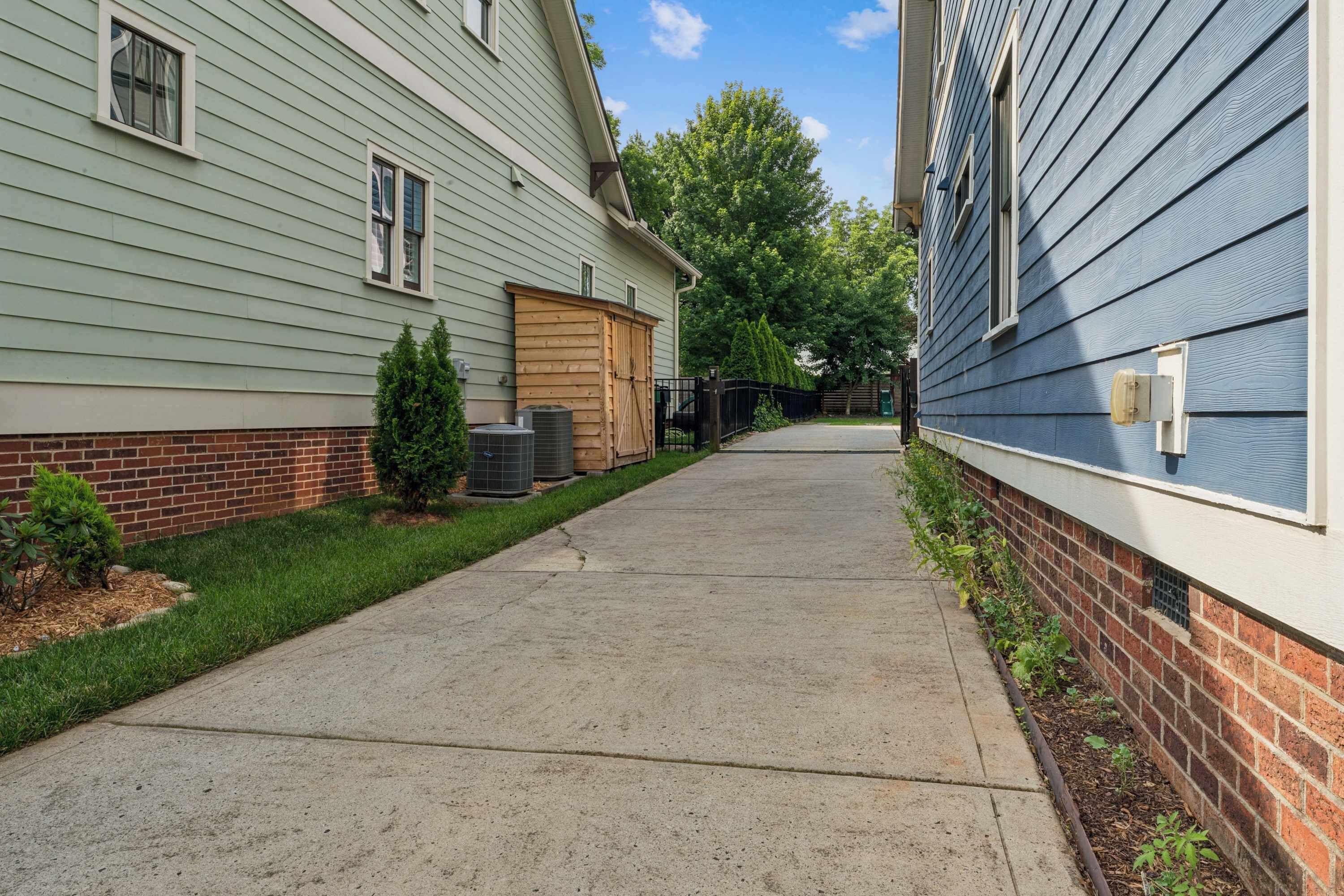 A residential street with two houses, a concrete sidewalk, and a small tree.