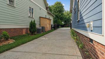 A residential street with two houses, a concrete sidewalk, and a small tree.