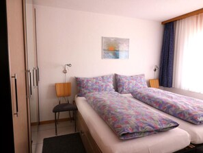 Ein Schlafzimmer mit Bett, Stuhl, Nachttisch, Lampe und einem Bild an der Wand.