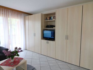 A living room with a flat-screen TV mounted on a cabinet, a sofa, and a small table with a vase of flowers. - Adlerhorst Leukerbad # 4-bed apartment, Dusche, WC by Interhome (Leukerbad)