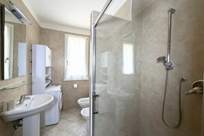 Een badkamer met een douchecabine van glas, een wastafel, toilet en een wasmachine.