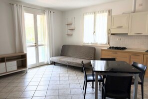 Une petite pièce propre, comprenant un canapé, une table à manger avec des chaises, un coin cuisine et une porte-fenêtre coulissante.