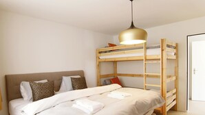 A bedroom with a bunk bed, a bedside table, a lamp, and a door. - Lorez 5D by Arosa Holiday Appartement/Fewo,  , 2-Bettwohnung Lorez 5D by Interhome (Arosa)