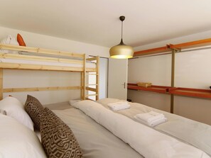 Ein Schlafraum mit Etagenbett, Holzleiter, Pendelleuchte und einem Kleiderschrank mit Spiegel.