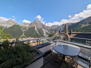 Eine Terrasse mit Tisch und Stühlen, mit Blick auf eine Berglandschaft unter blauem Himmel.