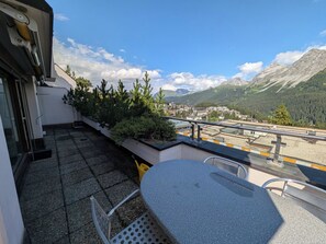 Ein Balkon mit Tisch und Stühlen, der auf eine gebirgige Landschaft mit einer Stadt in der Ferne blickt.
