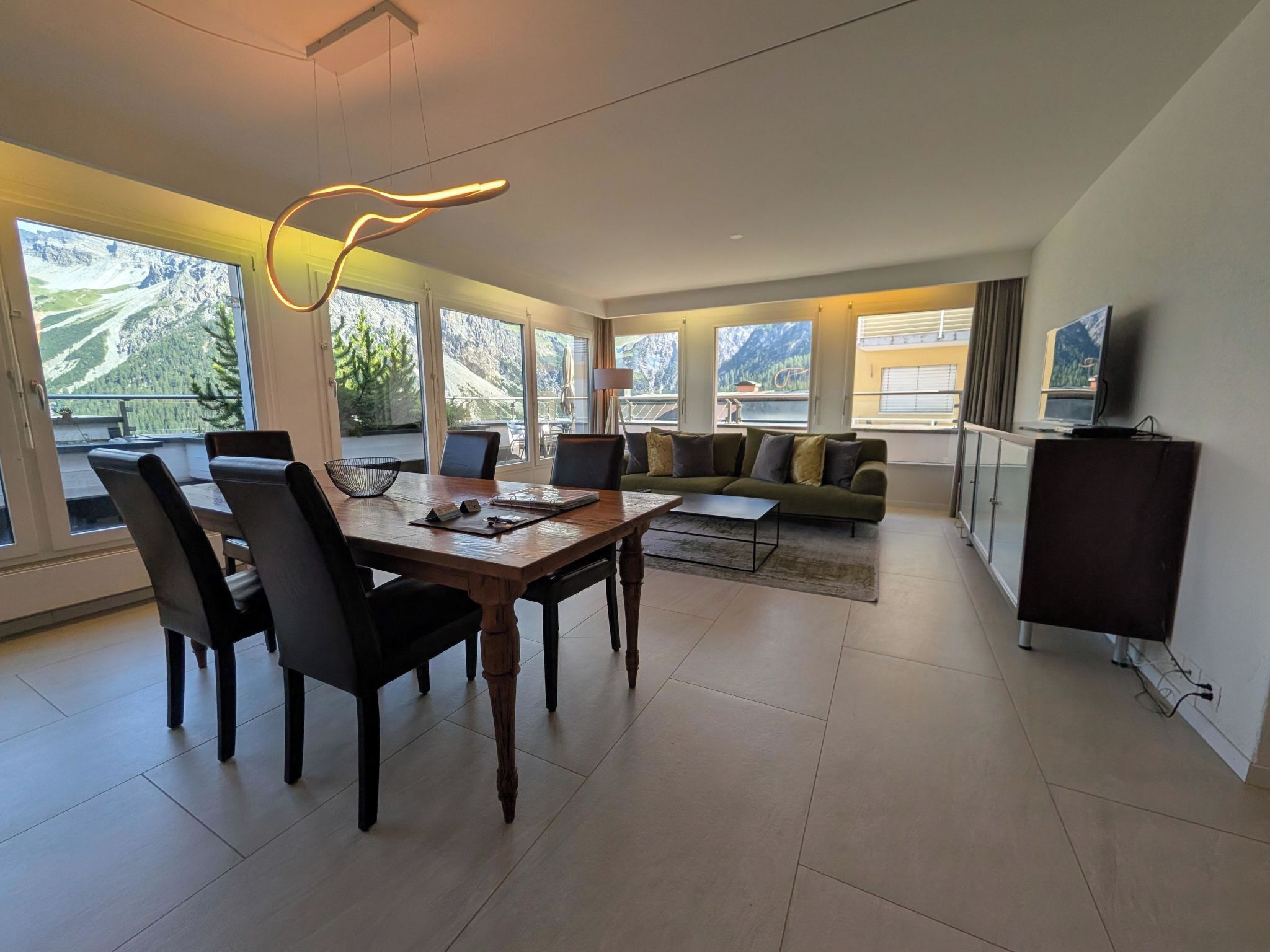 A modern hotel room with a dining area, a sofa, and a TV.