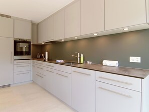 A modern kitchen with grey cabinets, a stainless steel oven, and a countertop with various items. - Lorez 5D by Arosa Holiday Appartement/Fewo,  , 2-Bettwohnung Lorez 5D by Interhome (Arosa)