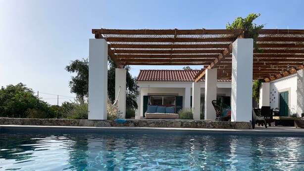Ein Schwimmbecken mit klarem Wasser, eine Pergola und ein Gebäude mit einem Ziegeldach.