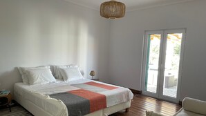 Ein Schlafzimmer mit einem Bett, einer Nachttischlampe, einem Sessel und Blick durch eine Tür.