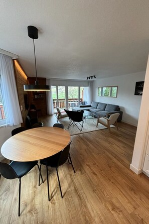 A modern living room with a wooden floor, a round table, and black chairs. - Edelweiss D 13 # 6-bed apartment, Dusche, WC 6-bed apartment, Dusche, WC by Interhome (Leukerbad)