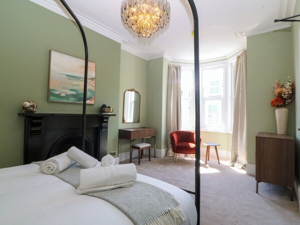 A bedroom with a four-poster bed, a fireplace, a desk, a chair, and a window with curtains. - Fox House (Llandudno)