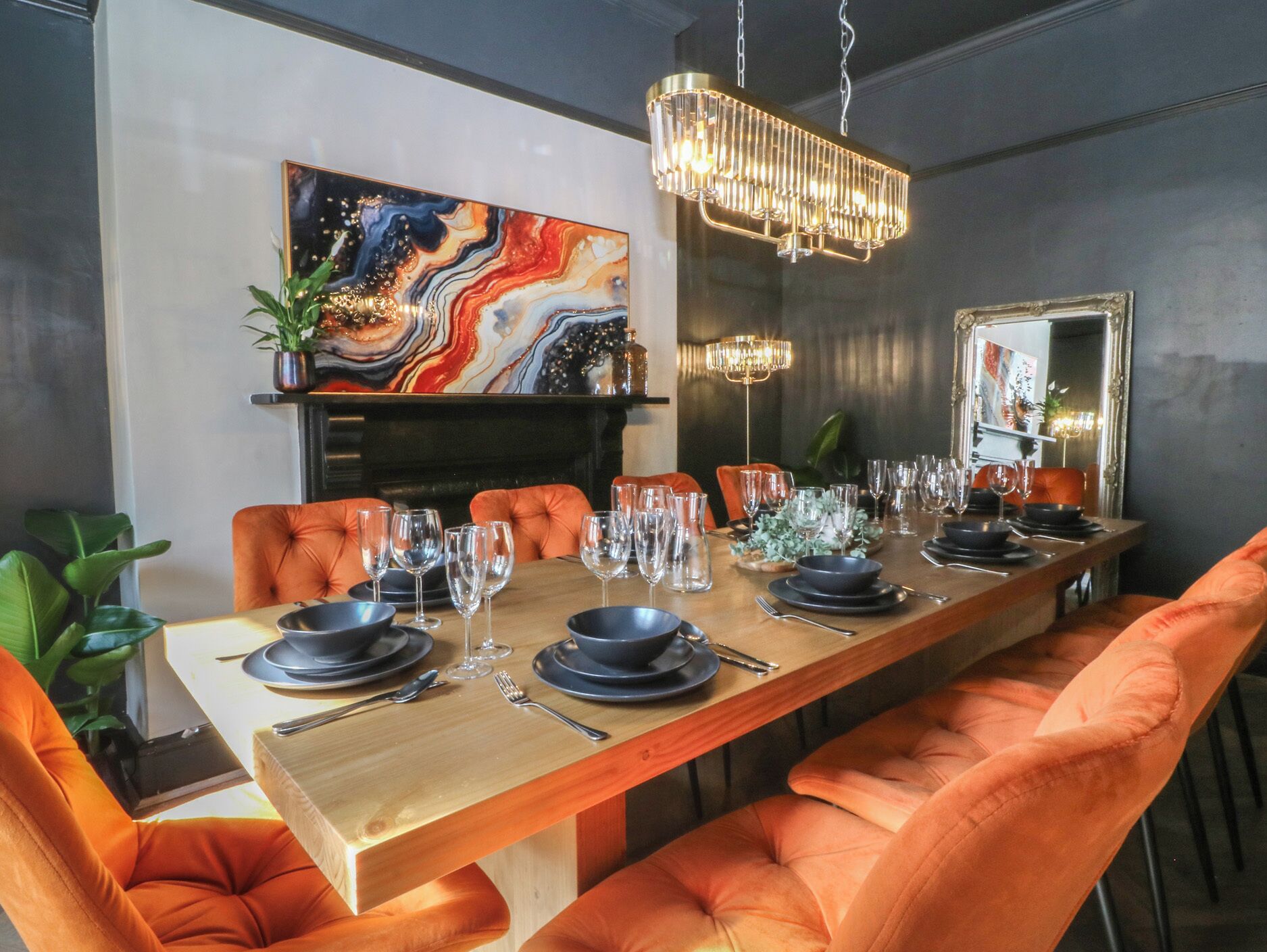 A dining area with a long table set for multiple guests, surrounded by orange upholstered chairs.