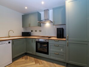 A compact kitchen with a dishwasher, oven, and microwave. - Fox House (Llandudno)