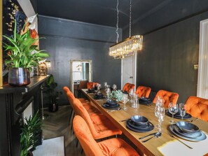 A dining area with a long wooden table set for a meal, surrounded by orange upholstered chairs. - Fox House (Llandudno)