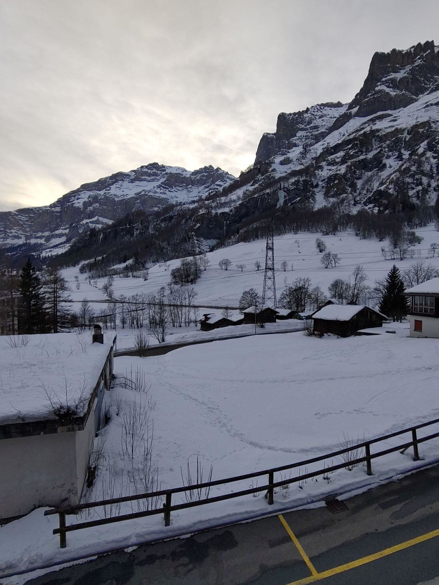 A snow-covered landscape with a mountain, a few buildings, and a road with a yellow line.
