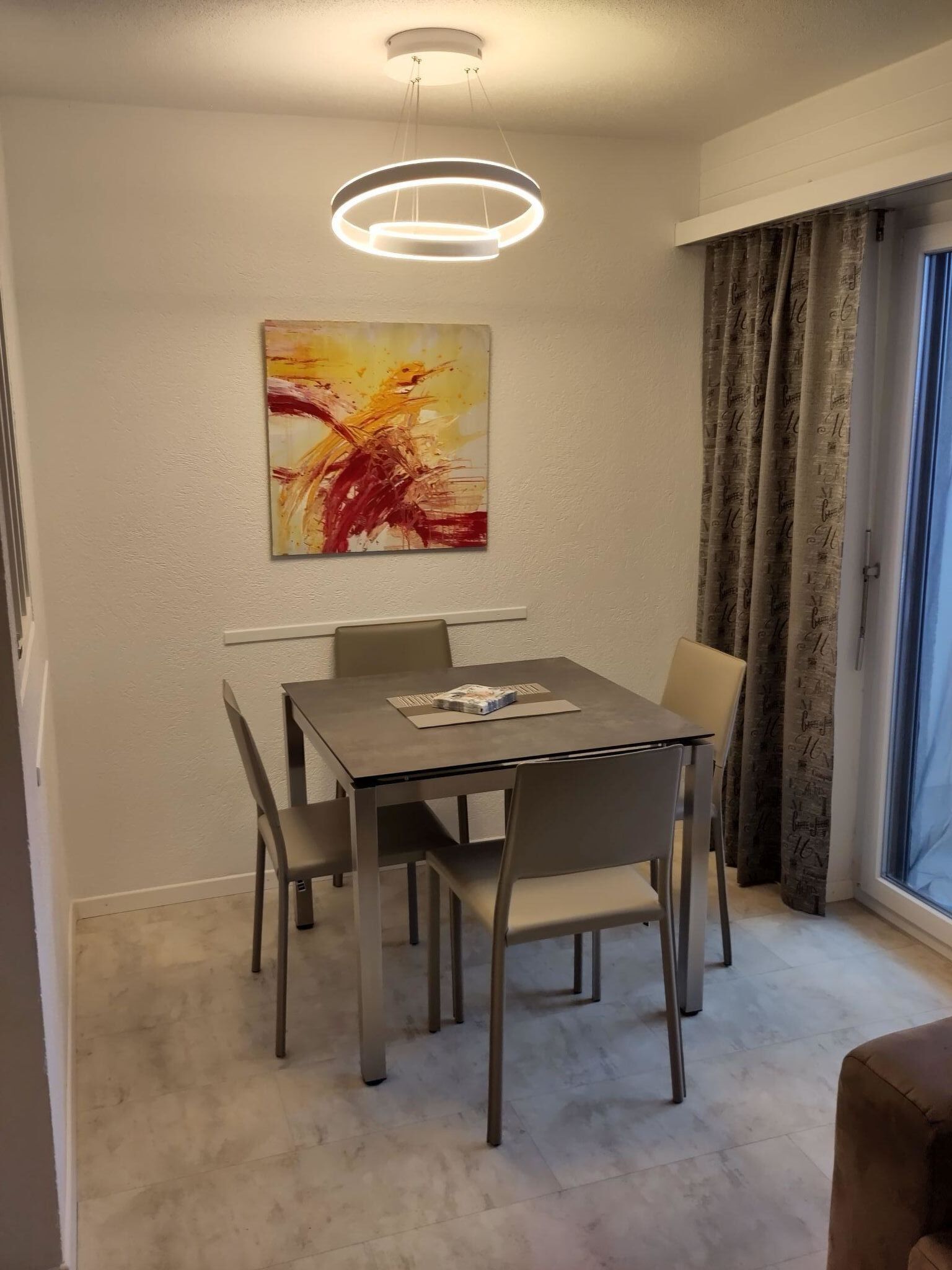 A dining area with a table, chairs, a modern pendant light, and a large abstract painting on the wall.