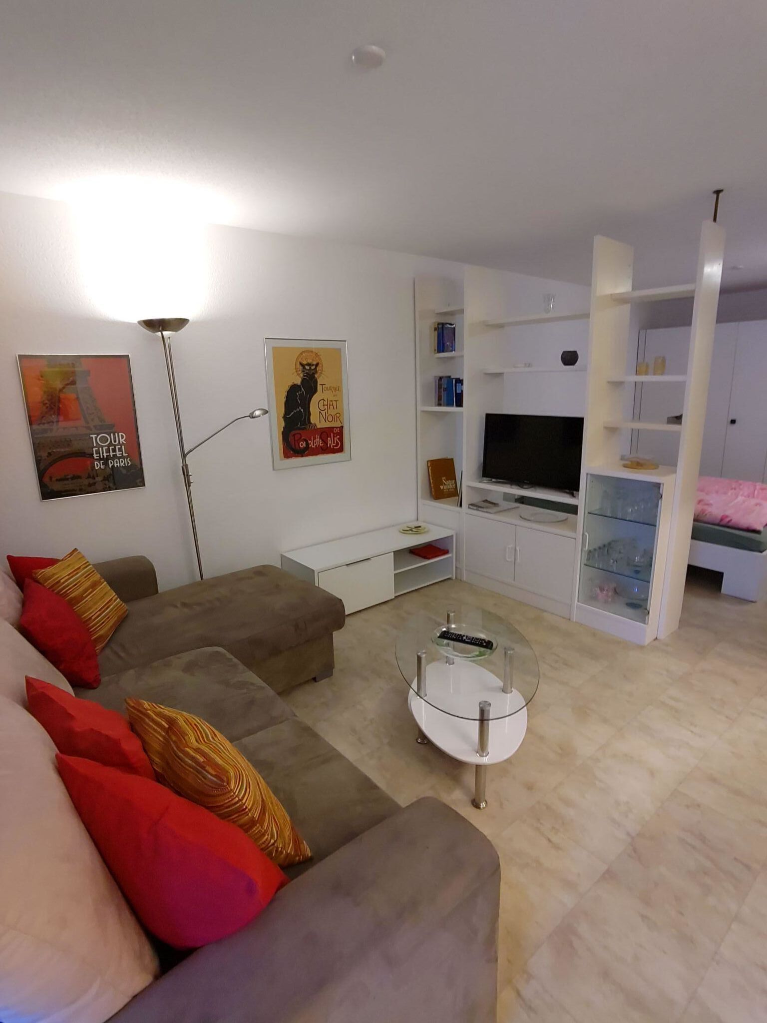 Ett modernt vardagsrum med en soffa, ett soffbord i glas, en tv och en bokhylla.