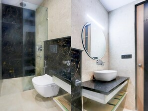Ein modernes Badezimmer mit Duschkabine aus Glas, einer weißen Toilette, einem Waschtisch aus schwarzem Marmor und einem großen Spiegel.