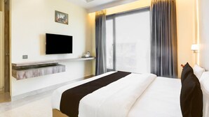 A hotel room with a bed, a flat-screen TV mounted on the wall, a window with curtains, and a small table with a cup and saucer. - Premium Townhouse Majra Isbt Dehradun (Dehradun)