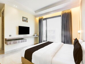 Ein Hotelzimmer mit Bett, einem an der Wand befestigten Flachbildfernseher, einem Fenster mit Vorhängen und einem kleinen Tisch mit Tasse und Untertasse.