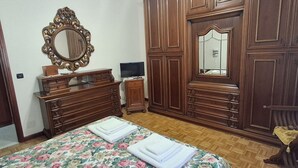 A bedroom with a wooden dresser, a large mirror, a television, and a bed with floral bedding.