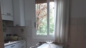 A kitchen with white cabinets, a dining table with chairs, a window with curtains, and a view of trees outside.