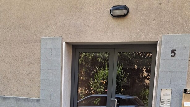 A building entrance with a glass door, a car parked outside, and a number '5' on the wall.